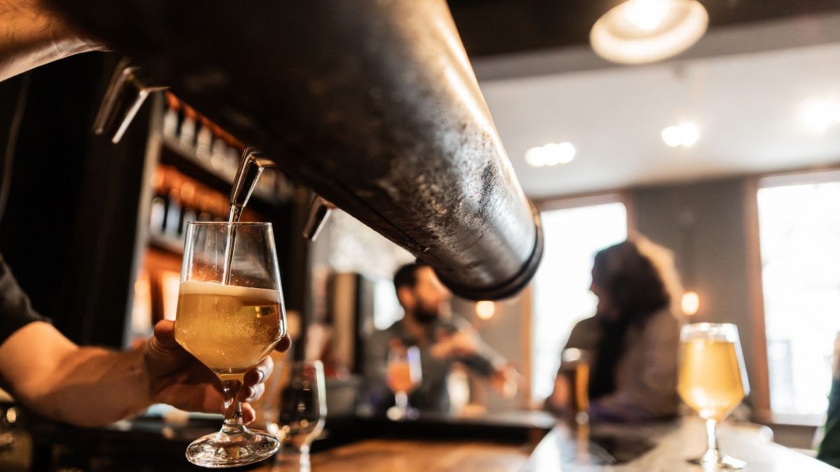 bartneder pouring beer with two people drinking in the background