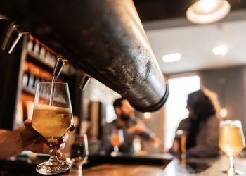 bartneder pouring beer with two people drinking in the background