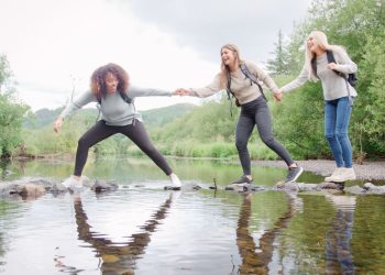 friends laughing while walking over stepping stones